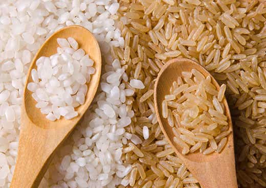 Piles of white and brown rice next to each other, with wooden spoons filled with rice lying on top.